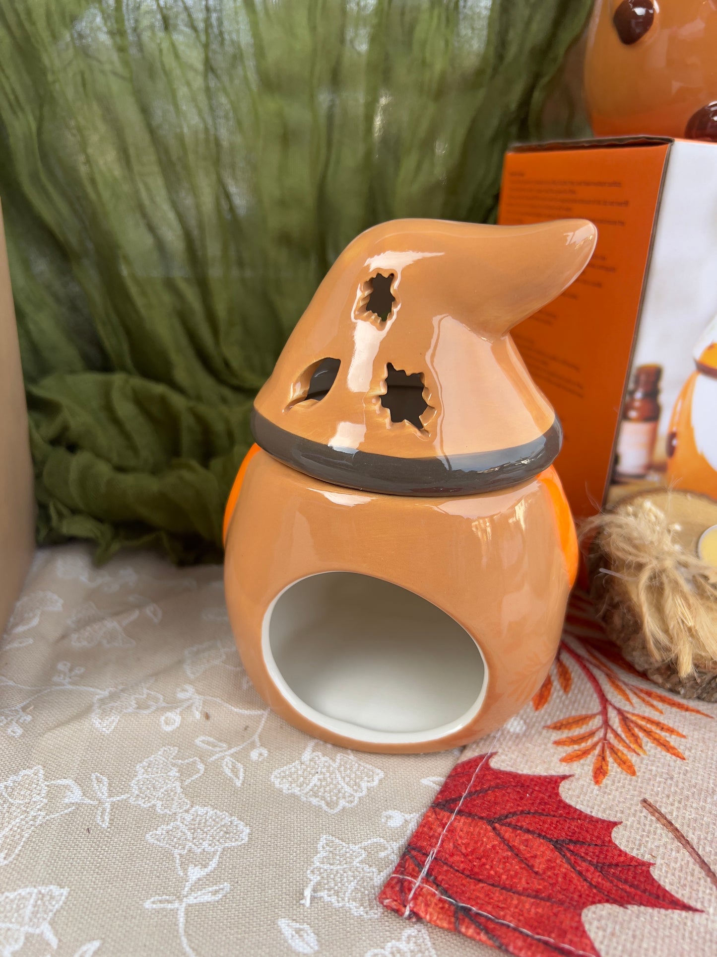 Ceramic gonk-shaped wax melt/oil burner with a lid on a textured surface with autumn leaves.