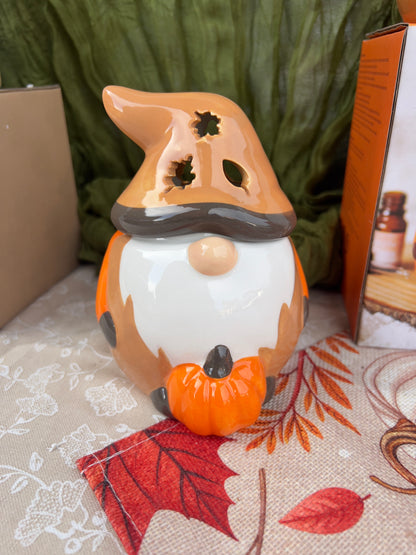 Decorative item shaped like a gonk with a pumpkin on its head, placed on a surface with a patterned cloth and leaves.