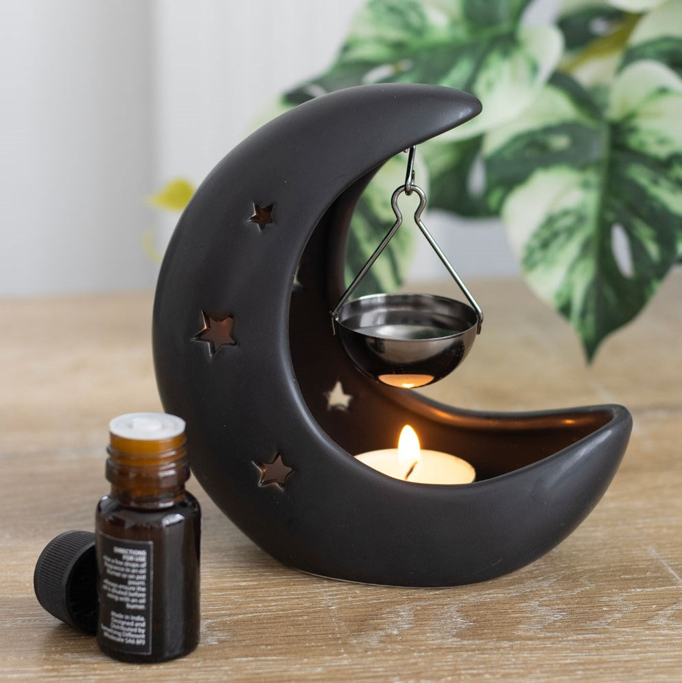 Black crescent moon hanging oil burner styled in a cosy home with glowing tealight and celestial décor